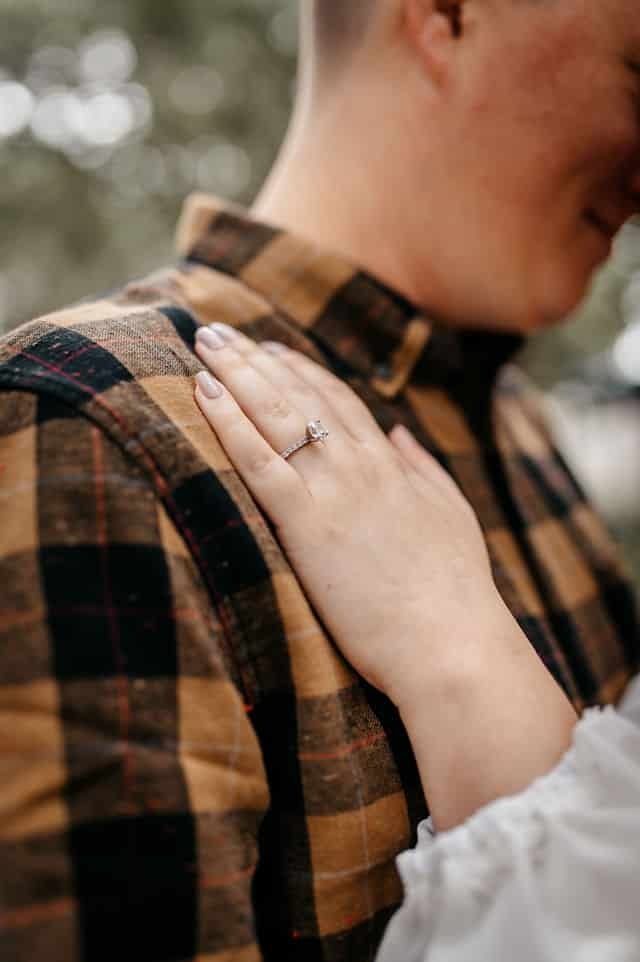 Close-up of an engagement ring, her hand resting on her fiance's shoulder.