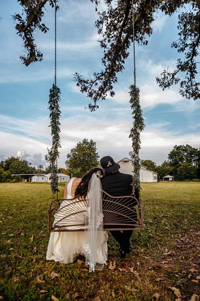A bride and groom sitting together on a rope swing hung from a moss-draped oak, her dress spread across the seat.