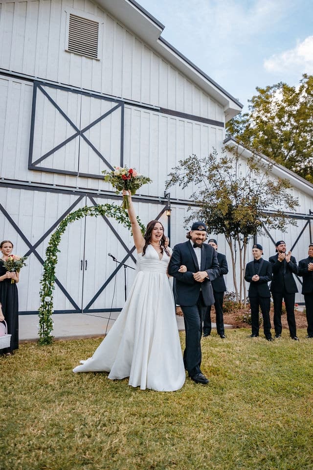 Bride and groom celebrating during an outdoor wedding ceremony beside a white barn in Georgia.