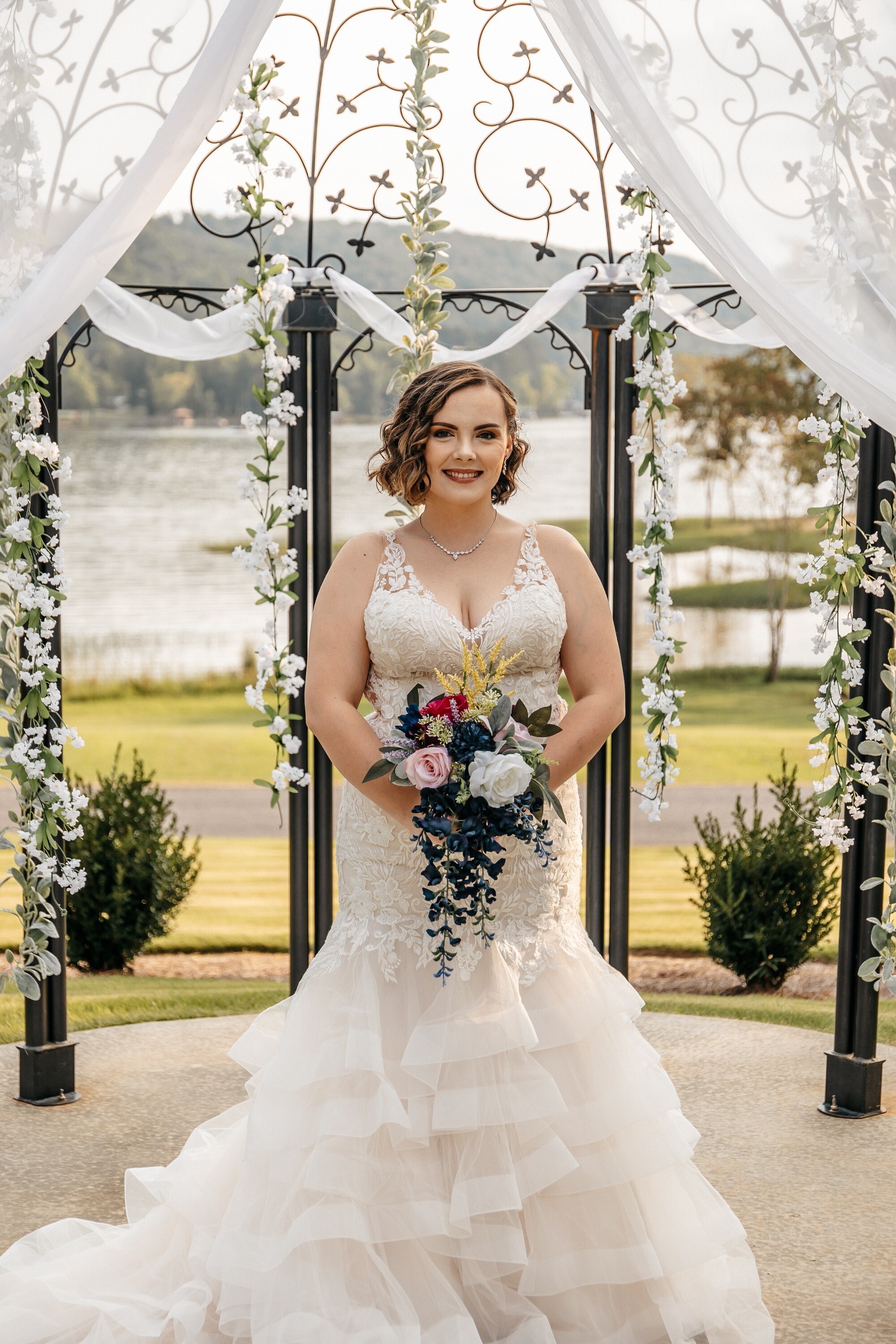 A bride poses in her white mermaid wedding dress under a pergola decorated with white flowers at one of many small outdoor wedding venues in georgia